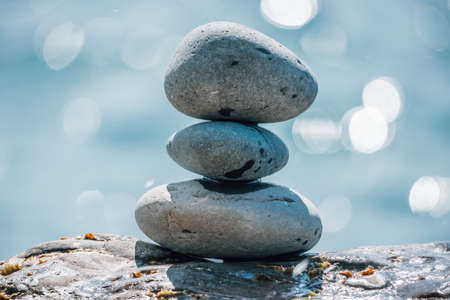 Balanced pebble pyramid on the beach on a sunny day. Abstract Sea bokeh on the background. Selective focus. Zen stones on the sea beach, meditation, spa, harmony, calmness, balance conceptの写真素材