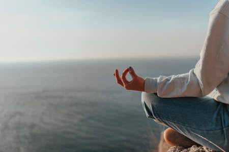 A young tourist Woman enjoying sunset over sea mountain landscape while sitting outdoor. Womens yoga...