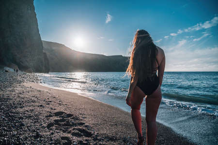 Selective focus. Happy carefree sensual woman with long hair in black swimwear posing at sunset beach. Silhouette of young beautiful playful positive woman outdoor. Summer vacation and trip conceptの写真素材
