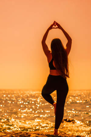 Woman makes heart with hands on beach. Young woman with long hair, fitness instructor, stretching...