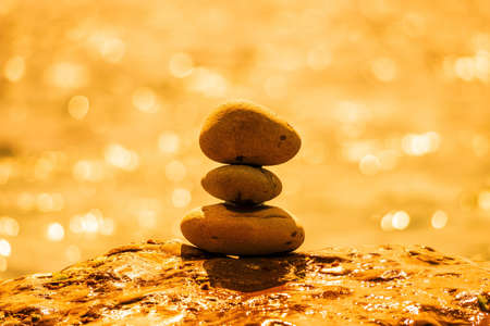 Balanced pebble pyramid on the beach on a sunny day. Abstract Sea bokeh on the background. Selective focus. Zen stones on the sea beach, meditation, spa, harmony, calmness, balance conceptの写真素材