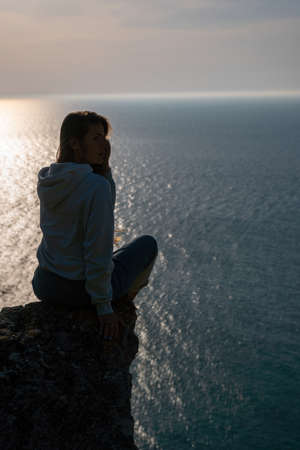 A young tourist Woman enjoying sunset over sea mountain landscape while sitting outdoor. Womens yoga fitness routine. Healthy lifestyle, harmony and meditationの写真素材