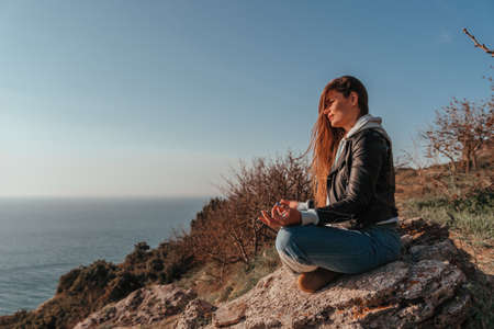 A young tourist Woman enjoying sunset over sea mountain landscape while sitting outdoor. Womens yoga fitness routine. Healthy lifestyle, harmony and meditationの写真素材