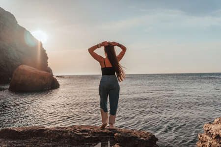 Young woman in swimsuit with long hair practicing stretching outdoors on yoga mat by the sea on a sunny day. Women's yoga fitness pilates routine. Healthy lifestyle, harmony and meditation concept.の写真素材