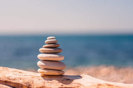 Balanced pebble pyramid on the beach on a sunny day. Abstract Sea bokeh on the background. Selective focus. Zen stones on the sea beach, meditation, spa, harmony, calmness, balance conceptの写真素材