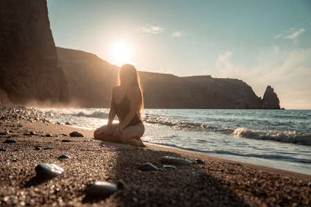 Selective focus. Happy carefree sensual woman with long hair in black swimwear posing at sunset beach. Silhouette of young beautiful playful positive woman outdoor. Summer vacation and trip conceptの写真素材