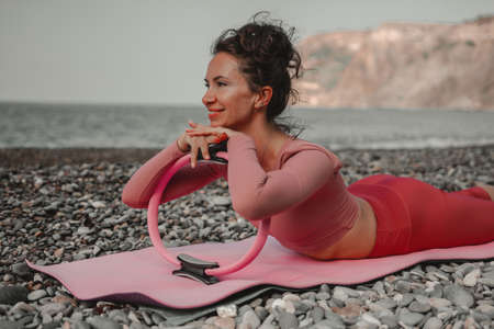Young woman with black hair, fitness instructor in pink sports leggings and tops, doing pilates on...