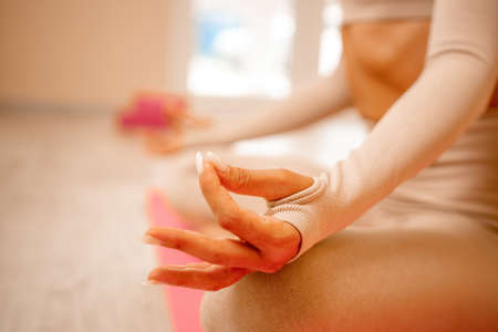 Young woman with long hair, fitness instructor in beige sportswear, preparing for stretching and pilates on yoga mat in the gym. Female fitness yoga concept. Healthy lifestyle harmony and meditation.の写真素材