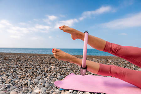 Young woman with black hair, fitness instructor in pink sports leggings and tops, doing pilates on...