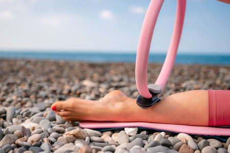 Young woman with black hair, fitness instructor in pink sports leggings and tops, doing pilates on...