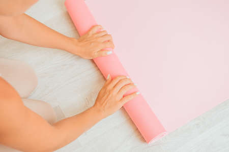Young woman with long hair, fitness instructor in beige sportswear, preparing for stretching and pilates on yoga mat in the gym. Female fitness yoga concept. Healthy lifestyle harmony and meditation.の写真素材