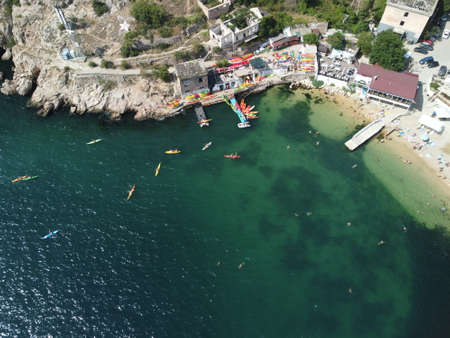 Aerial drone view on colorful kayaks grouped at a dock in sea bay. Group of happy kayakers are walking or training with instructor at sea bay. Active sea vacations conceptの写真素材