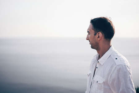 Digital nomad, man in the hat, a businessman with a laptop sits on the rocks by the sea during sunset, makes a business transaction online from a distance. Remote work on vacation.の写真素材