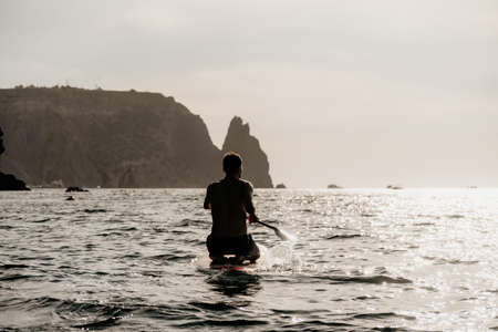 Side view foto of a man swiming and relaxing on the sup board. Sportive man in the sea on the Stand Up Paddle Board SUP. The concept of an active and healthy life in harmony with nature.の写真素材