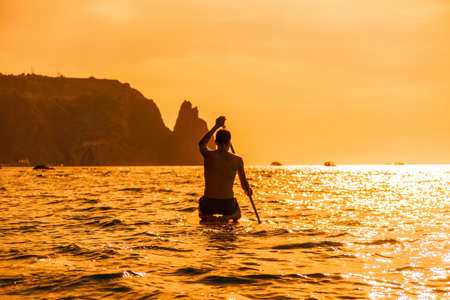 Side view foto of a man swiming and relaxing on the sup board. Sportive man in the sea on the Stand Up Paddle Board SUP. The concept of an active and healthy life in harmony with nature.の写真素材