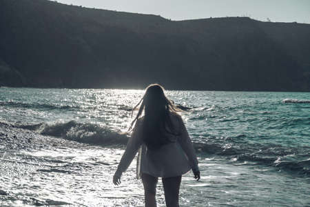 Selective focus. Happy carefree sensual woman with long hair in black swimwear posing at sunset beach. Silhouette of young beautiful playful positive woman outdoor. Summer vacation and trip conceptの写真素材