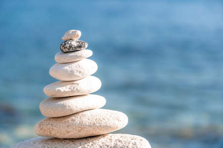 Pyramid stones on the seashore on a sunny day on the blue sea background. Happy holidays. Pebble beach, calm sea, travel destination. Concept of happy vacation on the sea, meditation, spa, calmness.の写真素材