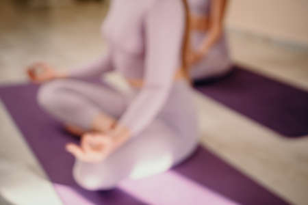 Abstract defocused foto of two young sporty woman, fitness instructor in pink sportswear doing stretching and pilates on yoga mat in the studio with mirror. Female fitness yoga routine concept.の写真素材