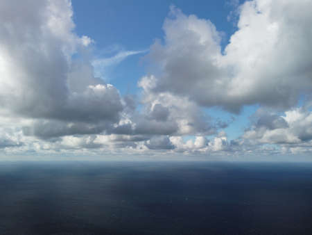 Abstract airy sky with moving plump clouds over the sea ocean. Small waves on clear water surface bokeh lights from sunrise. Holiday, vacation and recreational conceptの写真素材