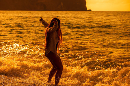 Selective focus. Happy carefree sensual woman with long hair in black swimwear posing at sunset beach. Silhouette of young beautiful playful positive woman outdoor. Summer vacation and trip conceptの写真素材
