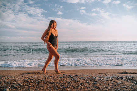 Selective focus. Happy carefree sensual woman with long hair in black swimwear posing at sunset...