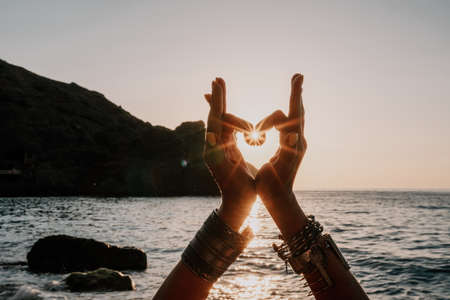 Middle aged well looking woman in white swimsuit and boho style braclets practicing outdoors on yoga mat by the sea on a sunset. Womens yoga fitness routine. Healthy lifestyle, harmony and meditationの写真素材