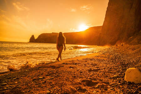 Selective focus. Happy carefree sensual woman with long hair in black swimwear posing at sunset...