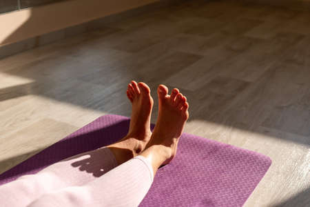 Young sporty woman, fitness instructor in pink sportswear doing stretching and pilates on yoga mat in the studio with mirror. Female fitness yoga routine concept. Healthy lifestyle and harmony.の写真素材