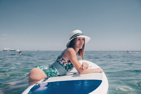 SUP Stand up paddle board. Young woman sailing on beautiful calm sea with crystal clear water. The...
