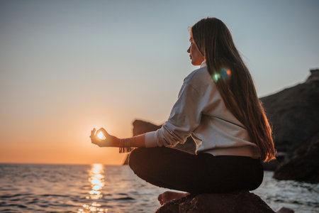 Young woman with long hair in sportswear and boho style braclets practicing outdoors on yoga mat by the sea on a sunset. Womens yoga fitness routine. Healthy lifestyle, harmony and meditationの写真素材