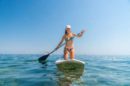 SUP Stand up paddle board. Young woman sailing on beautiful calm sea with crystal clear water. The concept of an summer holidays vacation travel, relax, active and healthy life in harmony with nature.の写真素材
