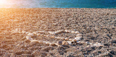 Love heart shape on sand made out of white pebbles, symbol of love on the beach with sea background....