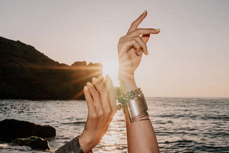 Middle aged well looking woman in white swimsuit and boho style braclets practicing outdoors on yoga mat by the sea on a sunset. Womens yoga fitness routine. Healthy lifestyle, harmony and meditationの写真素材