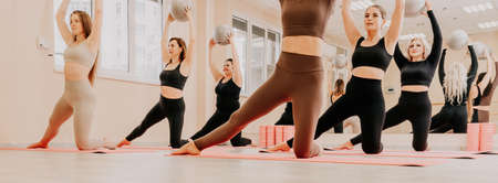 Group of middle aged women with fitness instructor in sportswear leggings and tops, doing Pilates...