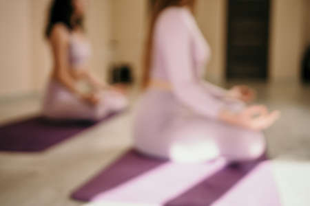 Abstract defocused foto of two young sporty woman, fitness instructor in pink sportswear doing stretching and pilates on yoga mat in the studio with mirror. Female fitness yoga routine concept.の写真素材