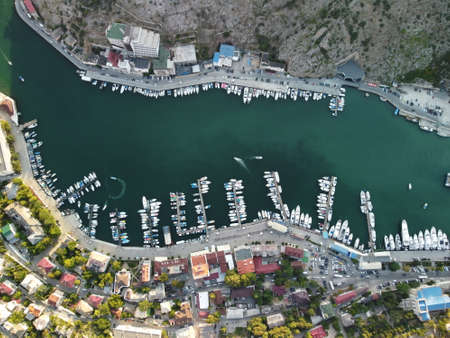 Aerial panoramic view of Balaklava landscape with boats and sea in marina bay on sunset time. Crimea Sevastopol tourist attraction. Drone top view shot of port for luxury yachts, boats and sailboatsの写真素材