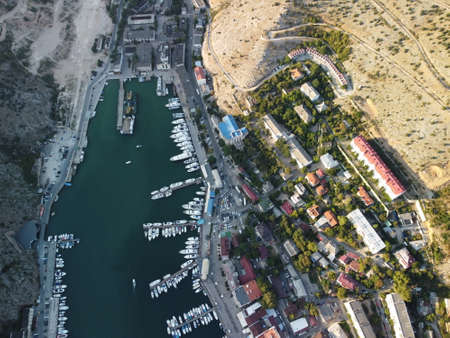 Aerial panoramic view of Balaklava landscape with boats and sea in marina bay on sunset time. Crimea Sevastopol tourist attraction. Drone top view shot of port for luxury yachts, boats and sailboatsの写真素材