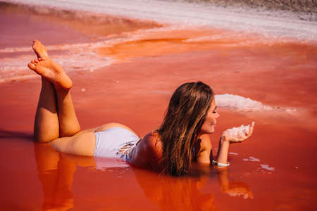 Young woman with long hair in pink salty lake with crystals of salt. Extremely salty pink lake,...