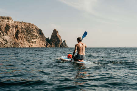 Side view foto of a man swiming and relaxing on the sup board. Sportive man in the sea on the Stand...