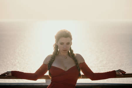 Closeup portrait of sensual young brunette woman in red dress, happily dancing outdoors isolated on blurry sea background with natural bokeh in soft warm sunset backlight. Selective focus.の写真素材