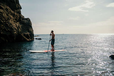 Side view foto of a man swiming and relaxing on the sup board. Sportive man in the sea on the Stand...
