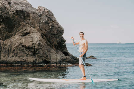 Side view foto of a man swiming and relaxing on the sup board. Sportive man in the sea on the Stand...