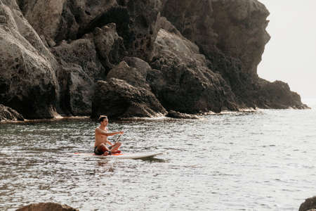 Side view foto of a man swiming and relaxing on the sup board. Sportive man in the sea on the Stand...