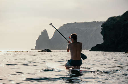 Side view foto of a man swiming and relaxing on the sup board. Sportive man in the sea on the Stand Up Paddle Board SUP. The concept of an active and healthy life in harmony with nature.の写真素材