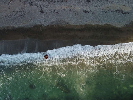 Aerial view from above on calm azure sea and volcanic rocky shores. Small waves on water surface in...