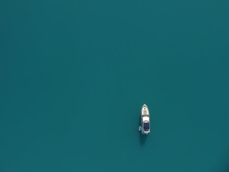 Aerial yacht on calm sea. Luxury cruise trip. View from above of white boat on deep blue water. Aerial top down view of rich yacht sailing sea. Summer journey on luxury ship.の写真素材
