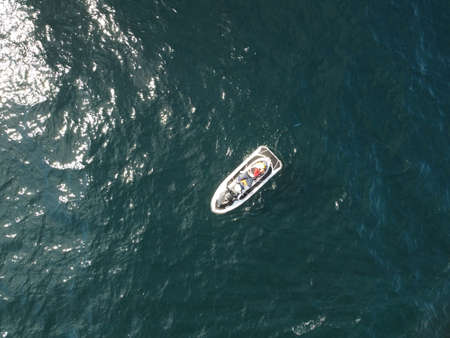 Happy people swim on air mattress behind a high speed water bike. Tourists ride on inflatable watercraft boat. Sea attraction. Water scooter skating people on large Inflatable raft. Aerial copter viewの写真素材