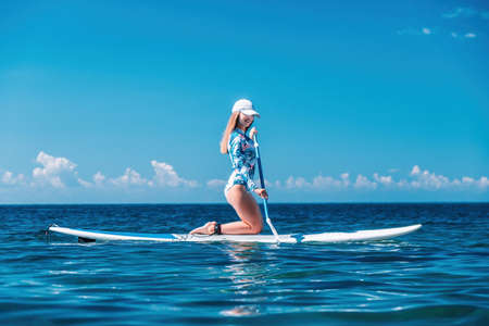 Woman sup sea. Happy healthy fit woman in bikini relaxing on a sup surfboard, floating on the clear turquoise sea water. Recreational Sports. Stand Up Paddle boarding. Summer fun, holidays travel.の写真素材