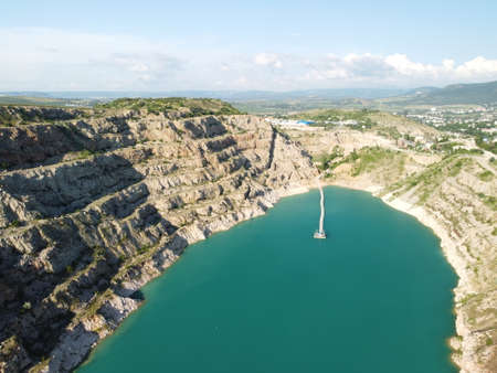 Aerial top view on opencast mining quarry with flooded bottom, turquoise surface of the lake. Quarry pond overgrown with green plants and clear turquoise waterの写真素材