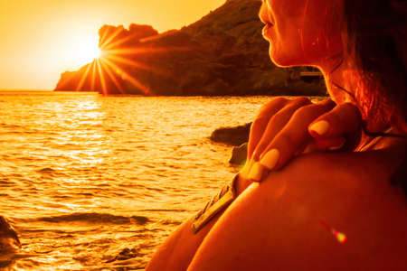 Middle aged well looking woman in white swimsuit and boho style braclets practicing outdoors on yoga mat by the sea on a sunset. Womens yoga fitness routine. Healthy lifestyle, harmony and meditationの写真素材